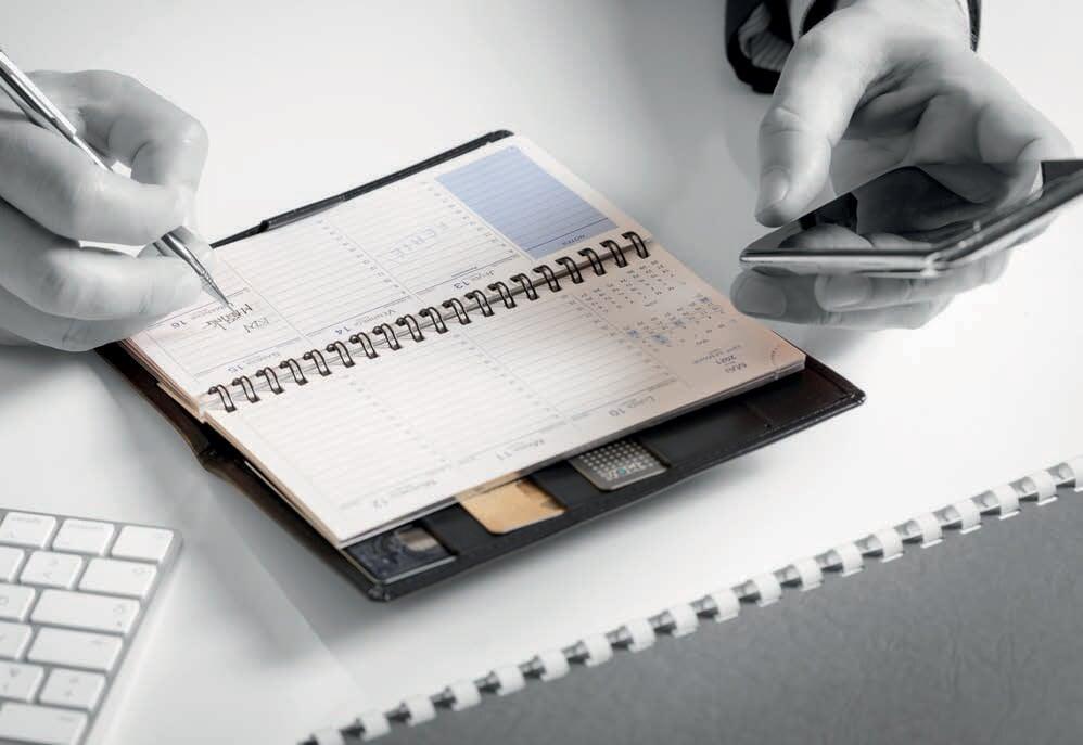 Une personne est en train de noter ses rendez-vous dans son agenda papier, qu’il aime avoir comme aide mémoire et support pour s’organiser au quotidien, en plus du smartphone.