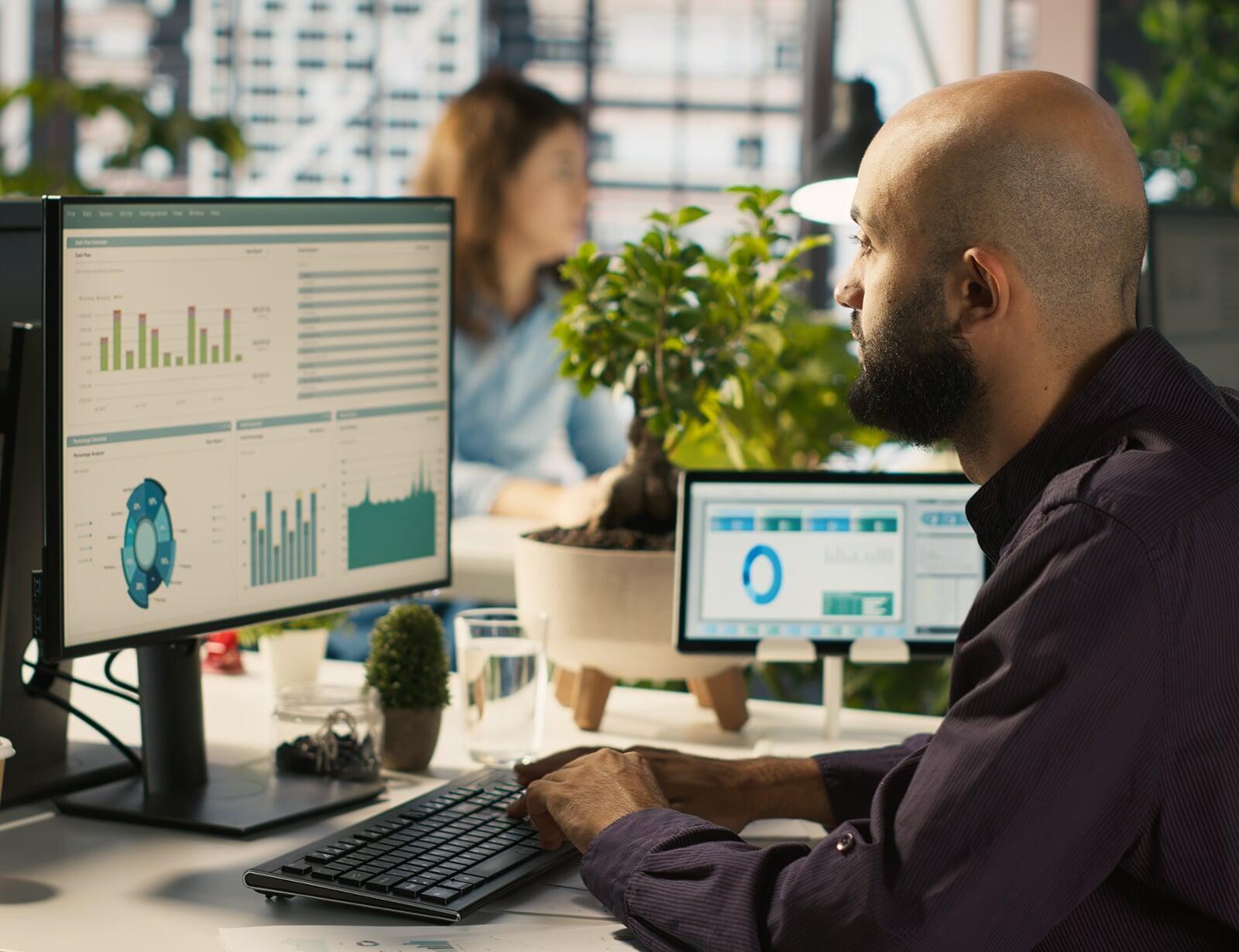 3 consultants, deux jeunes hommes et une jeune femme, sont assis autour d’une table, dans un openspace, et travaillent en équipe projet.