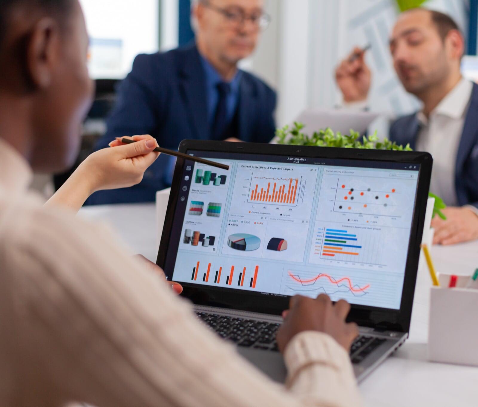 3 consultants, deux jeunes hommes et une jeune femme, sont assis autour d’une table, dans un openspace, et travaillent en équipe projet.